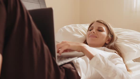 Happy Woman Lying at Hotel Room and Using Laptop