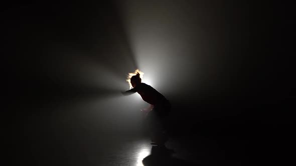 Muscular Female Practicing Capoeira in Darkness Against Spotlight in Studio