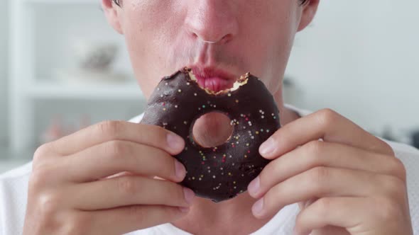 Man Eating Sweet Chocolate Donut Over White Interior Background