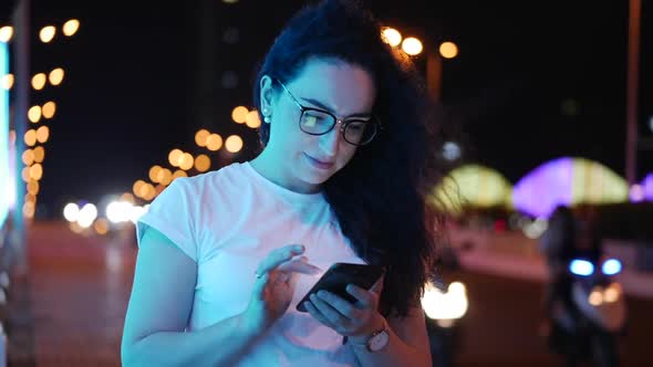 Pretty Woman Stands on the Street in a White T-shirt and Glasses, Makes Online Payments By Credit