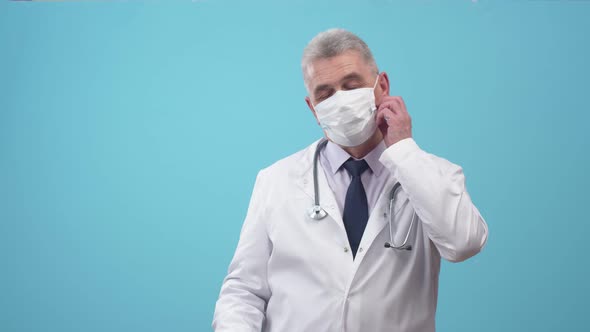 Adult Man Doctor Removes Goggles and Medical Mask Wiping Sweat From Forehead in the Studio