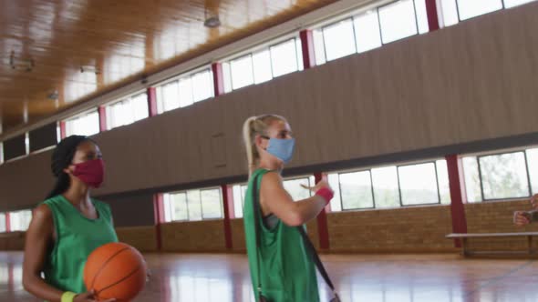 Diverse female basketball team greeting with elbows, wearing face masks