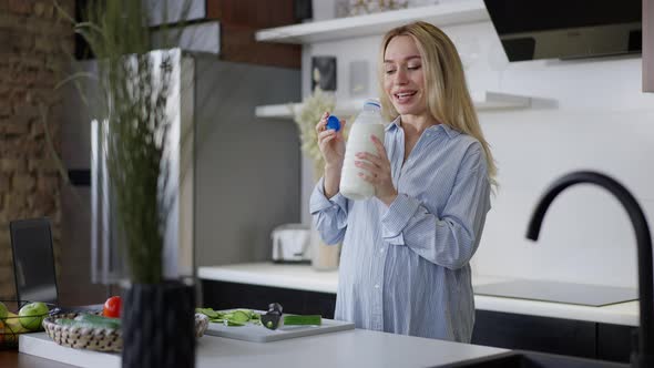 Portrait of Happy Pregnant Caucasian Woman Smelling Milk Smiling Standing in Kitchen at Home