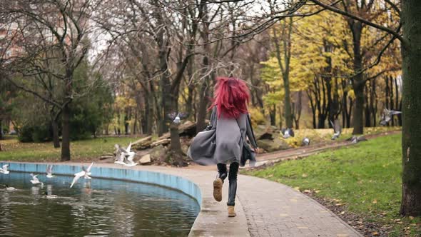 Back View of Attractive Woman with Red Hair Running Towards Pigeons and Making Them Fly Away in a