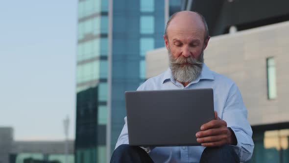 Happy Elderly European Senior Man Using Laptop Outdoor Making Payments Shopping Online