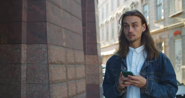 Happy Young Guy Looking at Smartphone Screen While Walking at Old City Street. Crop View of Bearded