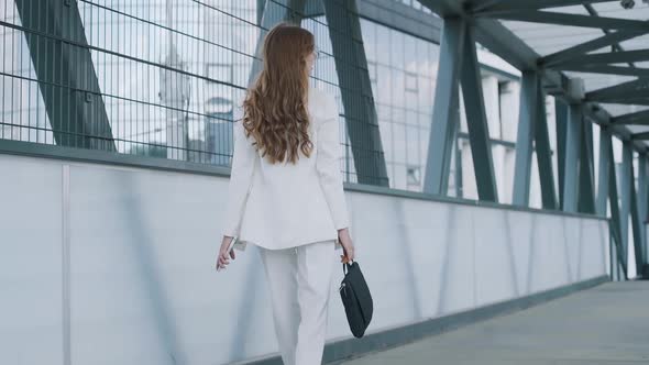 Young confident business woman in white suit walking with bag of laptop. Busy beautiful girl leaving