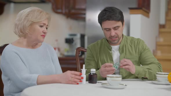 Senior Caucasian Woman Unwilling Take Medications Talking with Son Bringing Pills