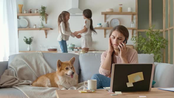 A Busy Mother Trying To Work Remotely at Home. On The Background Her Daughters Are Jumping Together