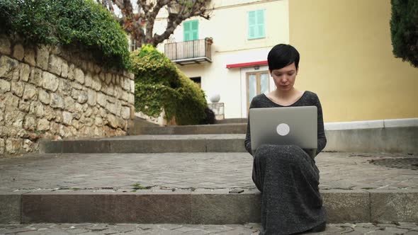 Beautiful Woman Sitting on the Stairs Using Computer in Front of the Color House