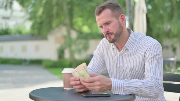 Middle Aged Man Counting Dollars While Sitting in Outdoor Cafe