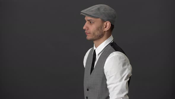 Portrait in Profile of Confident Mature Man in Vest and Flat Cap Showing Thumb Up Over Grey