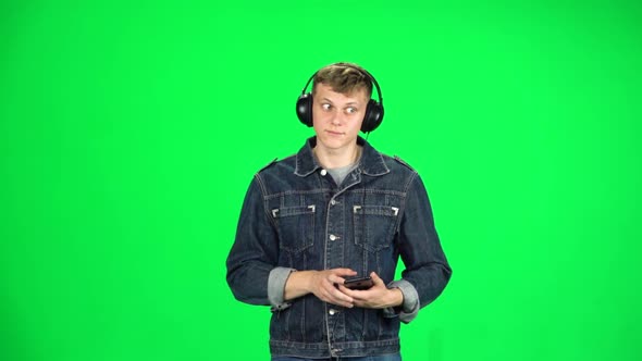 Guy in Big Headphones Goes, Listening Music and Dancing with Smartphone on Green Screen at Studio