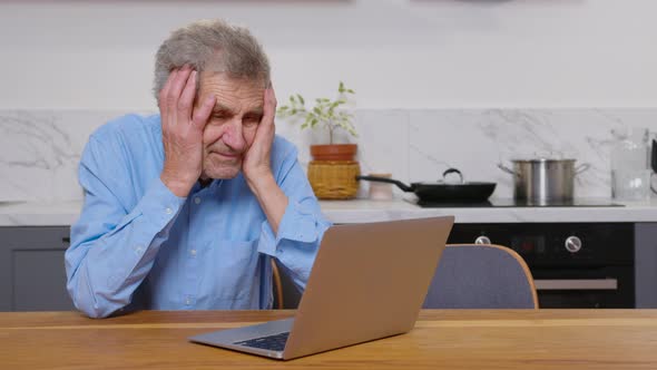 A Tired Broken Resigned Preoccupied Elderly Man Sits in Front of a Laptop Computer and Covers Face