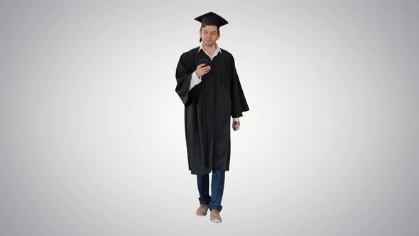 Male Student in Graduation Gown Checking His Phone While Walking on Gradient Background