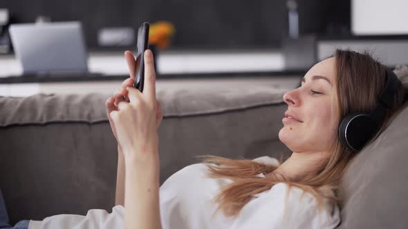 Woman Enjoying Her Free Time Laiyng on a Sofa with Music and Smartphone