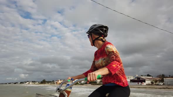 Closeup of mature woman riding a cruiser bicycle with a lighthouse and blue sky in the background.