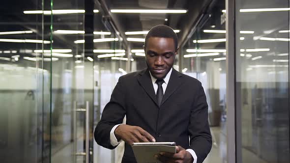 Businessman Walking to His Workplace Through Office Corridor, Using Tablet PC 