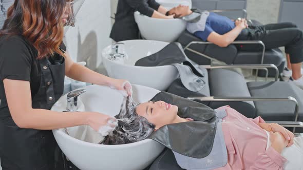 Asian woman customer lying down on salon washing bed getting hair washed in hair salon by stylist.