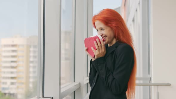 The Woman Received a Gift Box in the Form of a Heart. Happy Woman with Red Hair Rejoices at the Gift