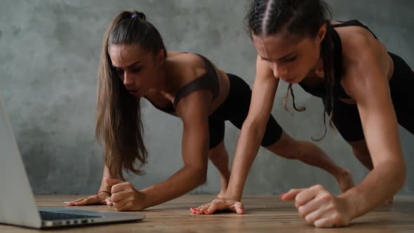 Young Sports Girls Twins Are Doing Sports Exercises Indoors at Home Using a Laptop Computer