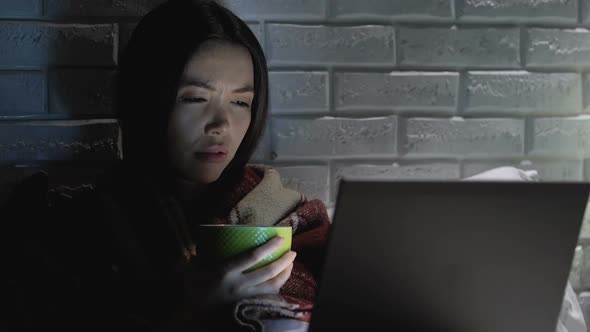 Ill Woman With Blanket Drinking Tea in Front of Laptop, Suffering From Headache