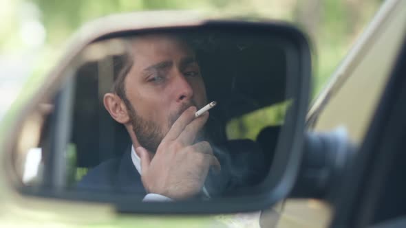 Reflection in Side View Mirror of Young Caucasian Man Smoking Cigarette Sitting on Driver's Seat in