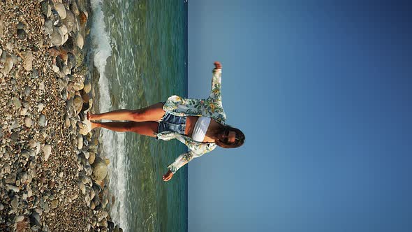 Carefree hipster surfer girl walking on pebble beach by the sea at windy day. Vertical video. 