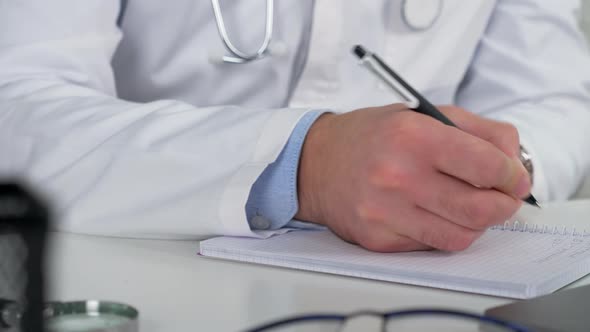Doctor writes symptoms in notebook examines patient online video call laptop