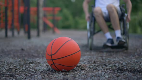 Orange Basketball Ball Lying on Sports Ground As Man Rolling Wheelchair From Background Lifting