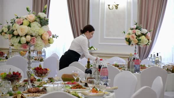 Girl Waiter Serves Food on a Festive Table