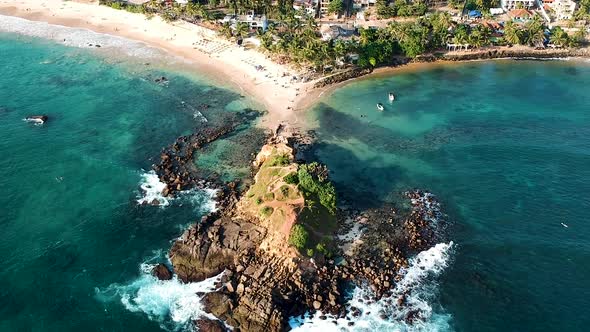 Aerial drone of Mirissa Beach at sunset golden hour. Parrot Rock with waves on sandy beach. Mirissa,