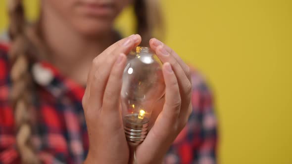 Closeup Lamp Turning on in Teenage Caucasian Hands at Yellow Background