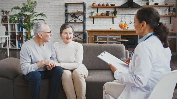 Doctor Woman Announcing Good Test Results to an Elderly Couple Who Rejoicing Sitting on Couch During