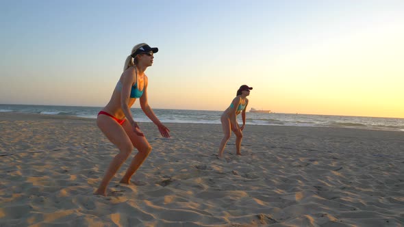 Women teams play beach volleyball at sunset and a player passes the ball.