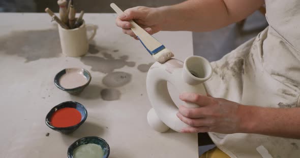 Mid section of female potter wearing apron using glaze brush to paint on pot at pottery studio