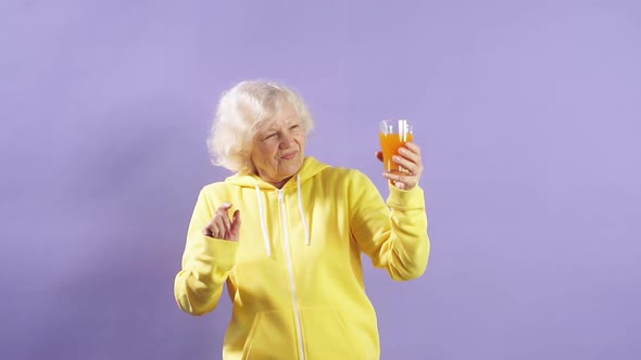 Cheerful Old Lady in a Yellow Sweater Dances and Drinks Fresh Carrot Juice