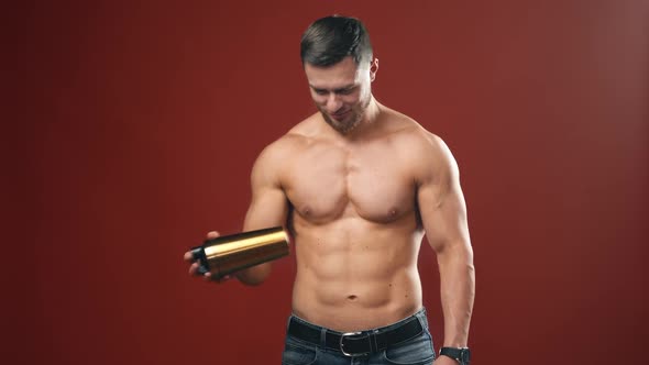 Muscular sportsman in red studio. Smiling bodybuilder mixing flask