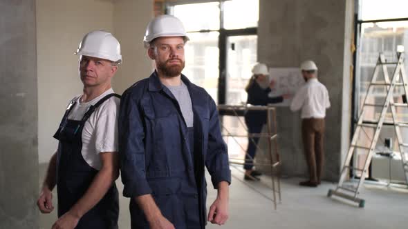 Two Builders in Helmets Posing at Work Place