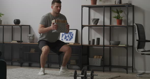 Athletic Man Is Squatting with Books in Hands in Room Strength Training for Keeping Fit Home Fitness