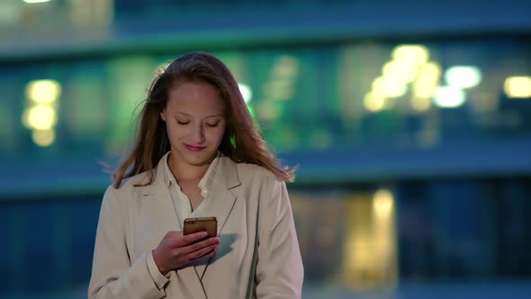 Young Girl at Night Reads Message on the Smartphone.