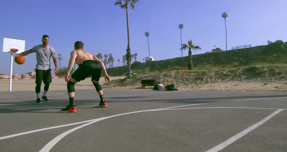 A man dribbles while playing one-on-one basketball hoops on a beach court