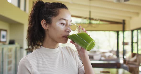 Relaxed biracial woman with vitiligo drinking healthy smoothie in kitchen