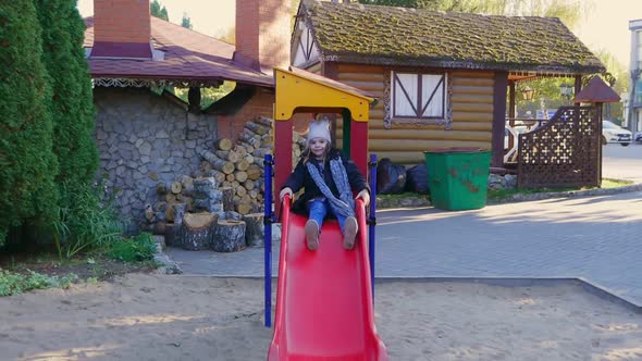 Cute Kid Girl Slide on a Children Playground and Laughs