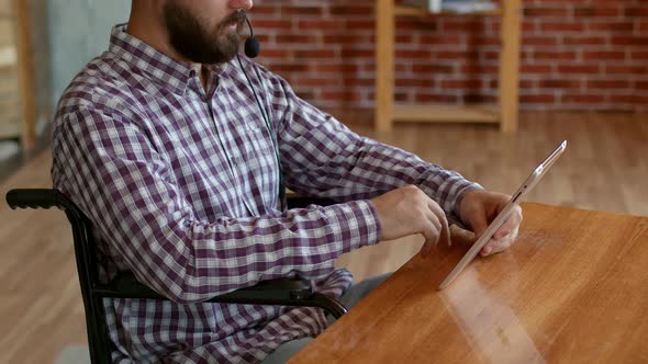 Disabled Freelancer with Headset and Tablet Sits in Wheelchair and Works in Support Service Side