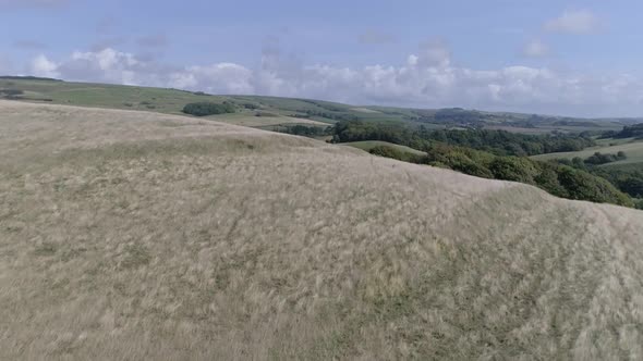 Low tracking aeriales forward fast up above a hill to reveal the village of Abbotsbury, in the Dorse