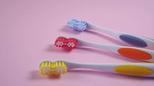 Three bright toothbrushes on a delicate pink background. 