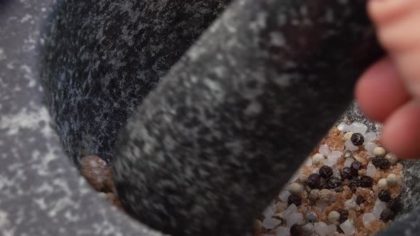 Closeup of Pestle Crushing and Mixing Salt and Peppers in the Grey Stone Mortar