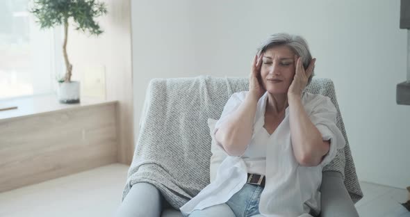 Older Attractive Woman Massaging Her Temples and Leaning Back in Her Chair Pleasantly Relaxing