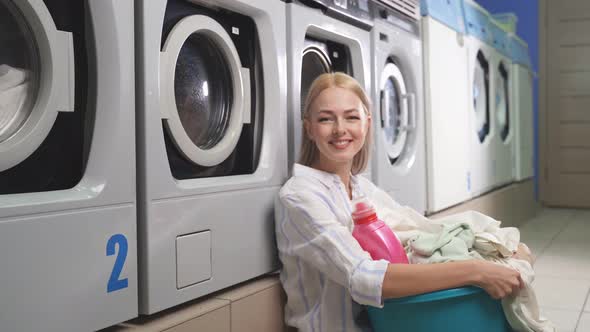 Portrait of an Attractive Blonde Woman in a Public Laundry Room Next To a Washing Machine Holding a